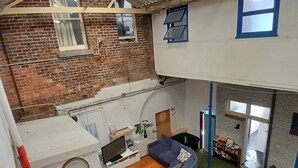 A loft-style living area with a high ceiling, exposed brick walls, and a green carpet. - 1849 Backpackers Hotel (Albany)