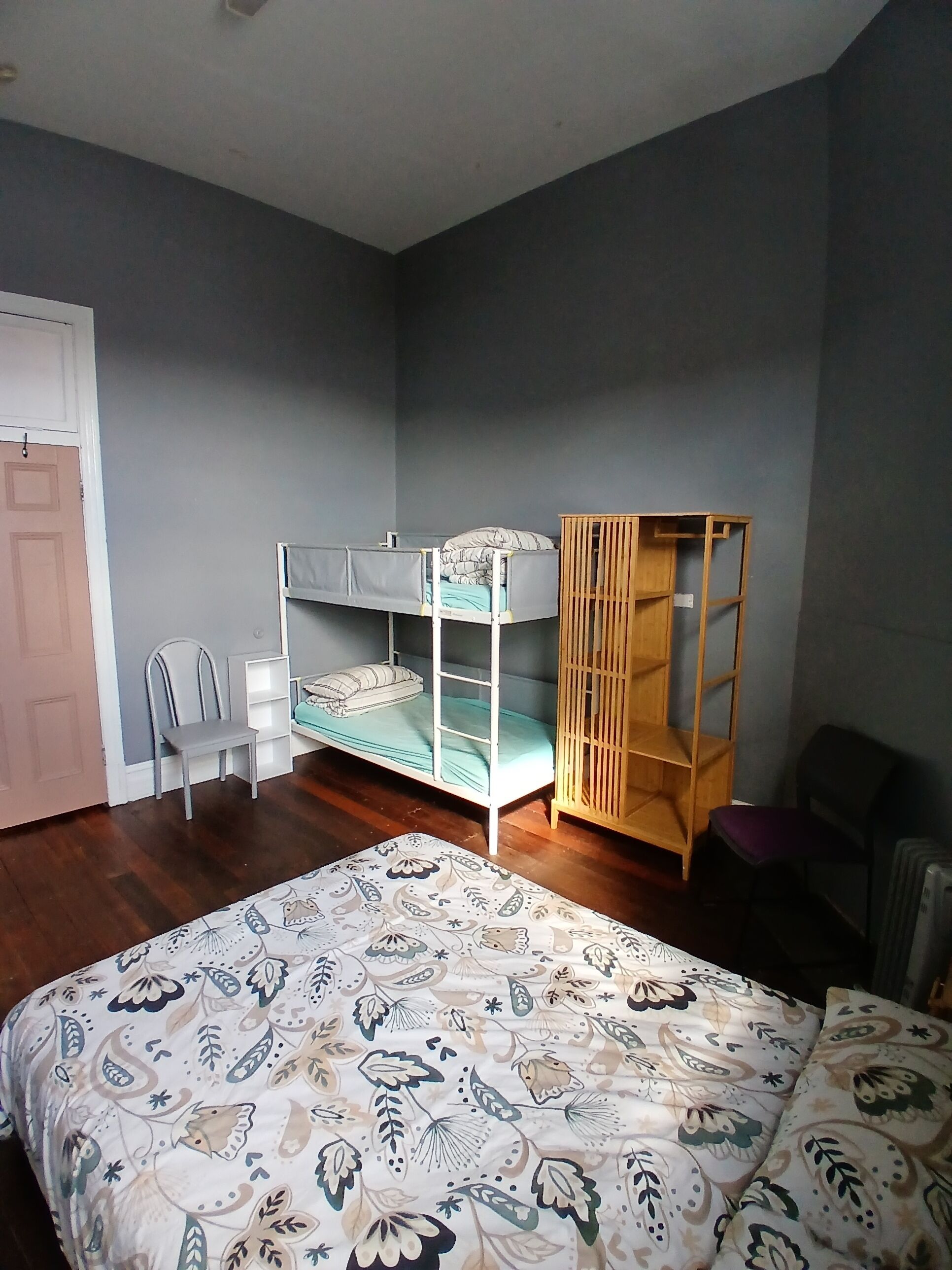 A bedroom with a bunk bed, a wooden cabinet, a chair, and a patterned bedspread.