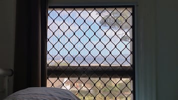 A bedroom with a bed, a window with a metal screen, and a view of the outdoors.
