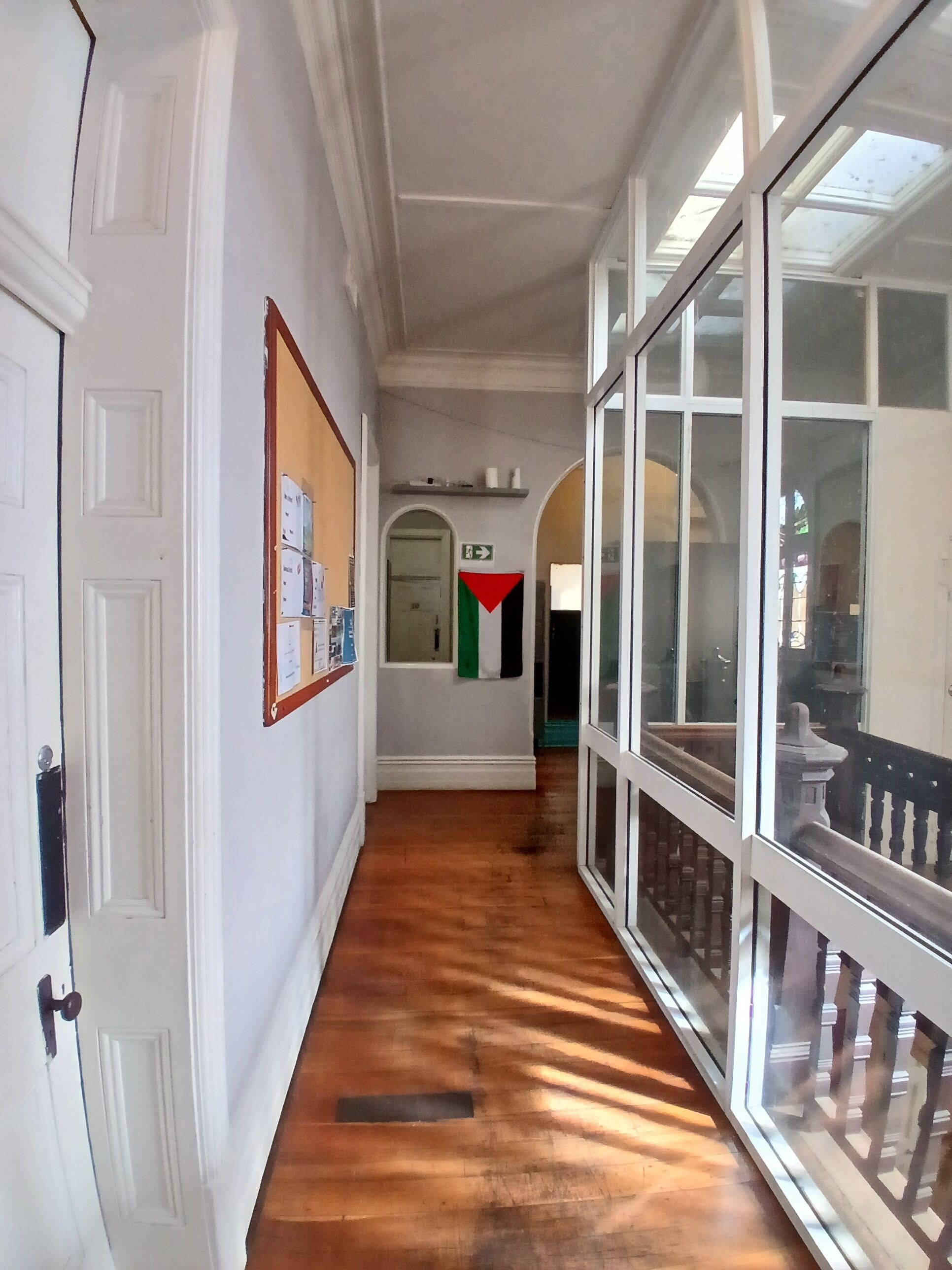A corridor with white walls, a wooden floor, and a glass door leading to a balcony.