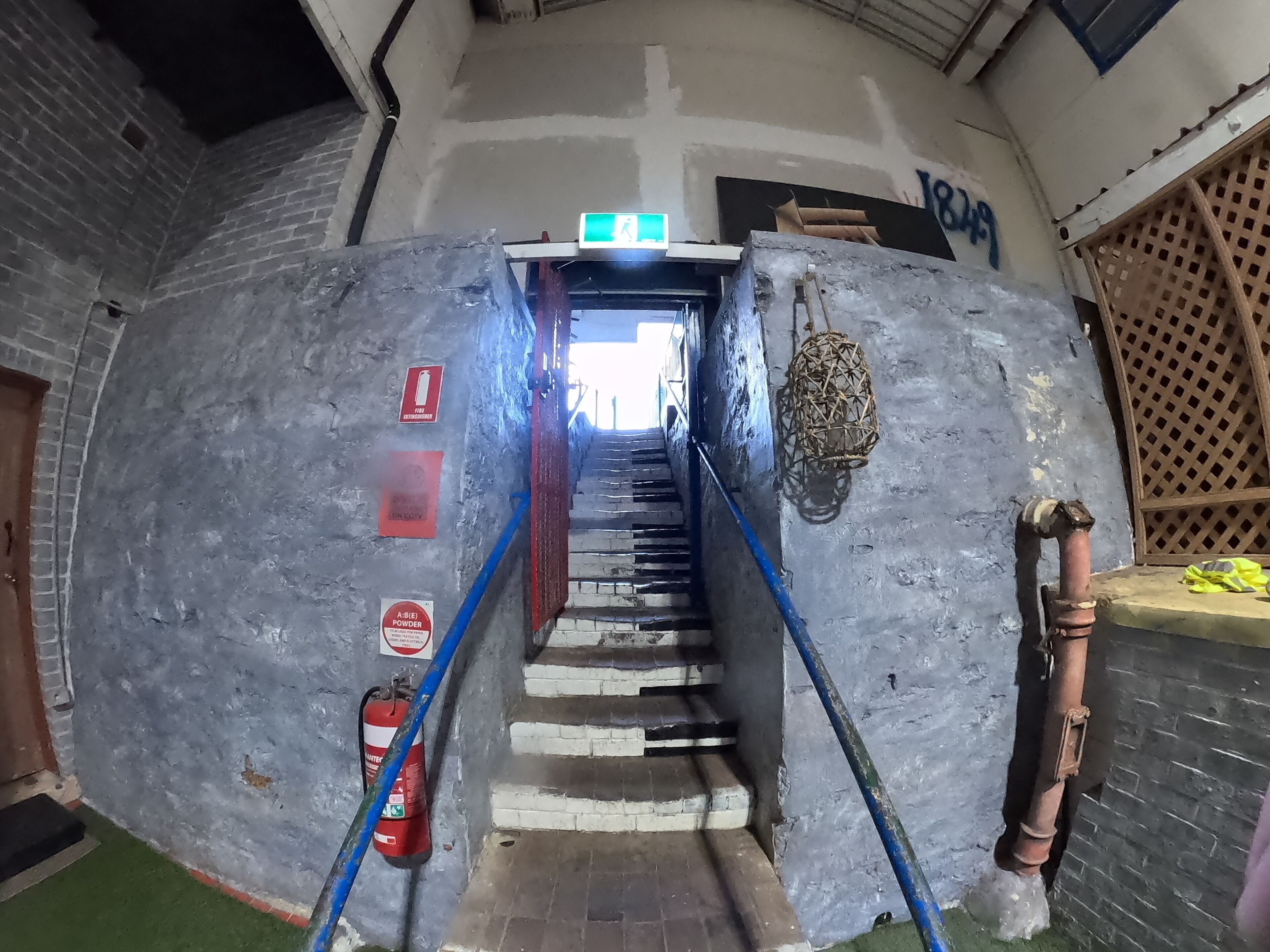 Una escalera que conduce a un nivel superior, con extintor y botiquín en la pared.