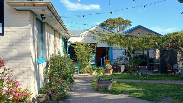 A residential area with a paved walkway, a house with a blue roof, and string lights. - 1849 Backpackers Hotel (Albany)