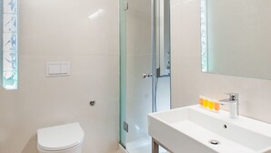 Un baño moderno con cabina de ducha de vidrio, lavamanos blanco y un inodoro.
