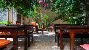 Un patio acogedor con muebles de madera y suelo estampado, rodeado de exuberante follaje y una pared rústica.