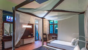 Una cama con dosel y cuatro columnas con vistas al exterior, un pequeño escritorio y una silla.