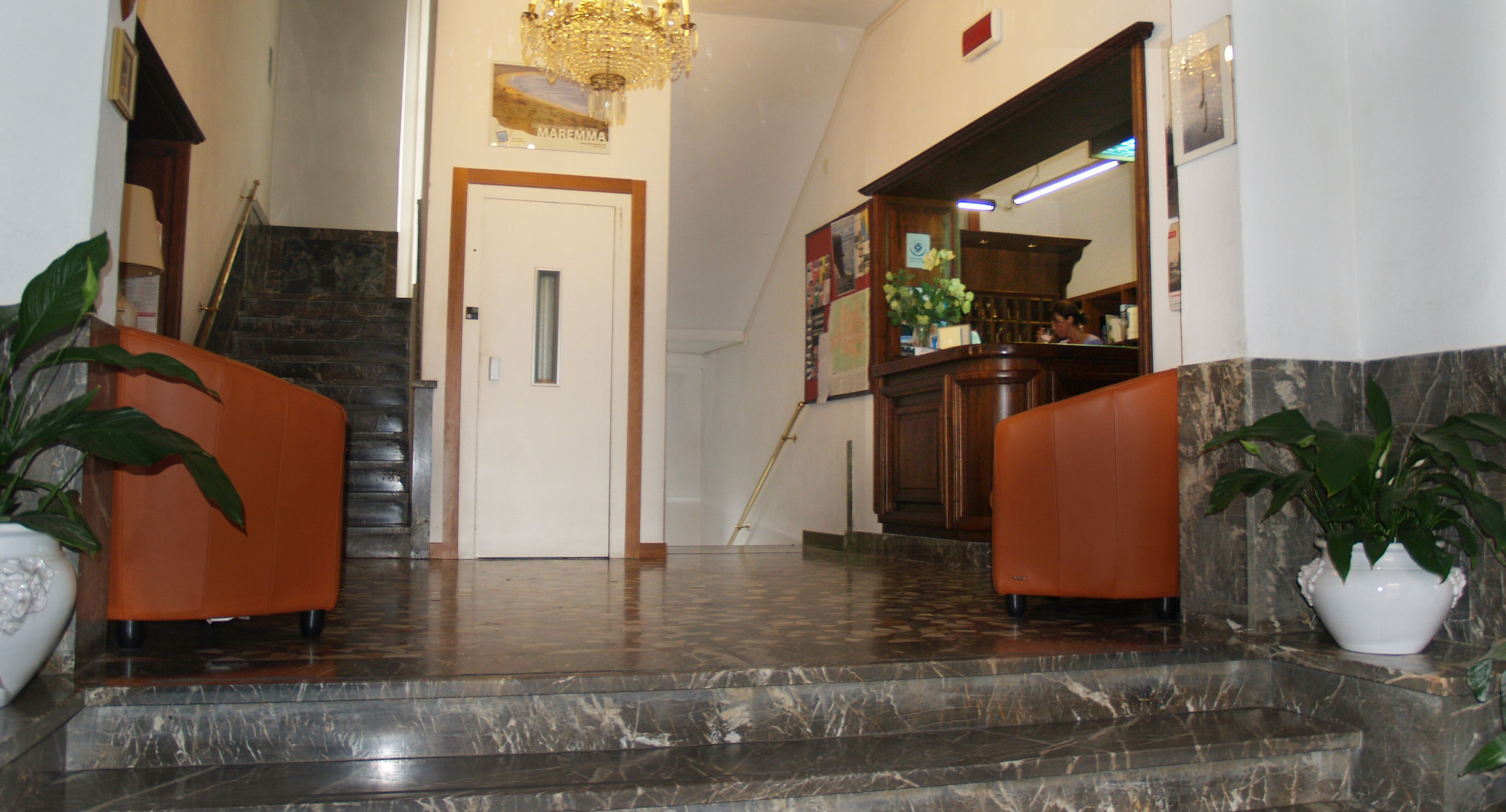Un'accogliente hall d'albergo con pavimento in marmo, una scalinata e due divani arancioni.