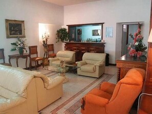 Uma sala de estar com sofá, poltronas, mesa de centro e um espaço de jantar com armário e cadeiras.
