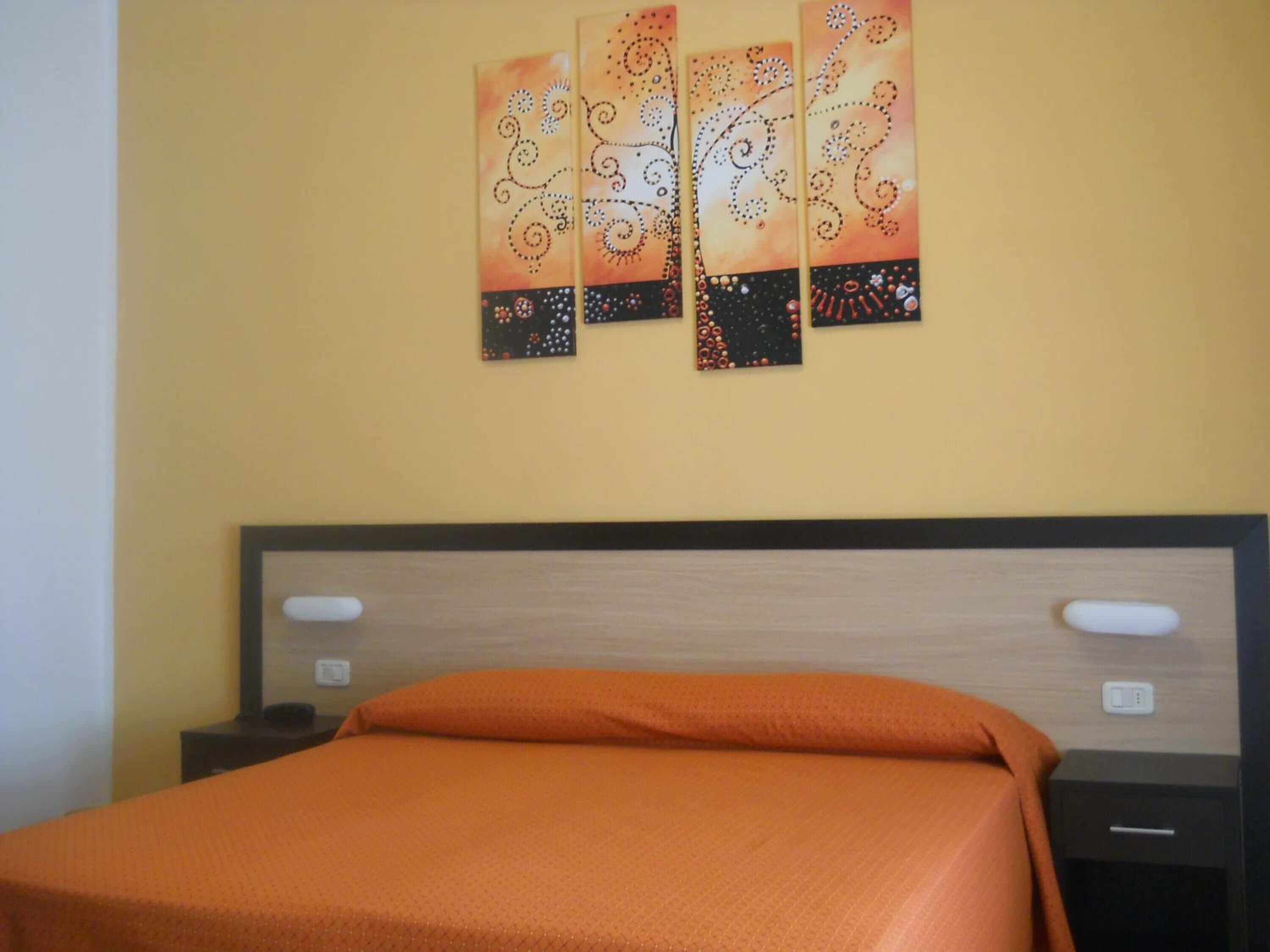 A hotel room with a bed, a nightstand, and a wall-mounted artwork.