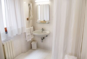 Uma casa de banho com uma sanita branca, uma pequena estante de vidro acima, um espelho, um suporte para toalhas e um radiador.