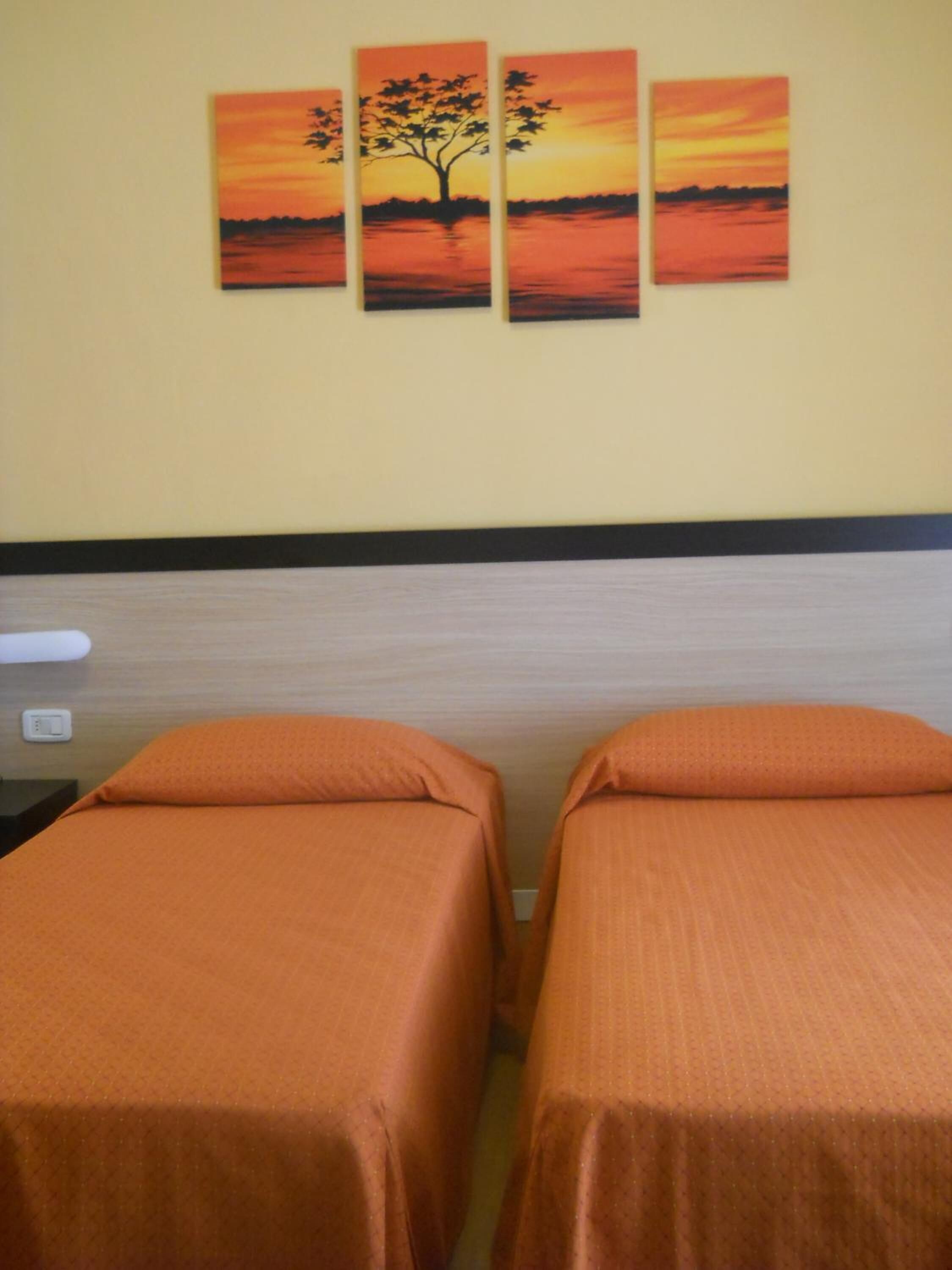 Habitación de hotel con dos camas individuales, un cuadro colgado en la pared de un atardecer y una pared lisa.