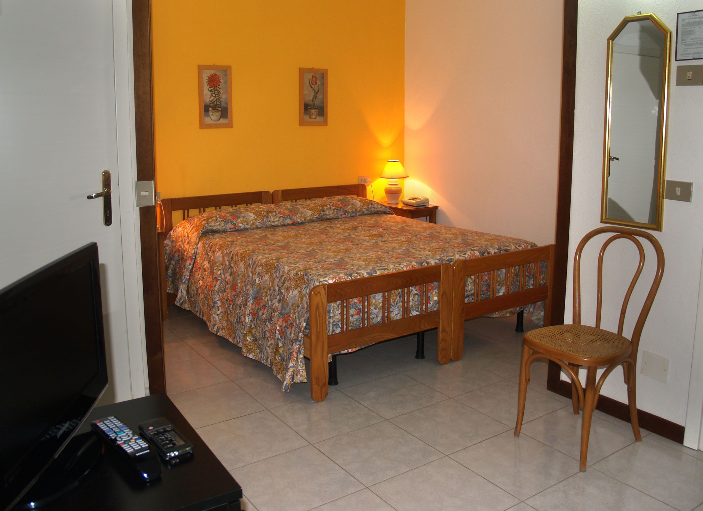 A bedroom with a bed, a chair, a nightstand with a lamp, and a television.