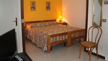 A bedroom with a bed, a chair, a nightstand with a lamp, and a television.
