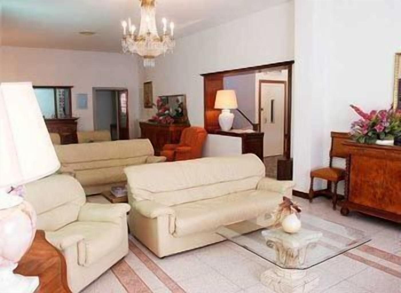 A living room with a beige sofa, a small table with a vase, and a wooden sideboard with flowers.
