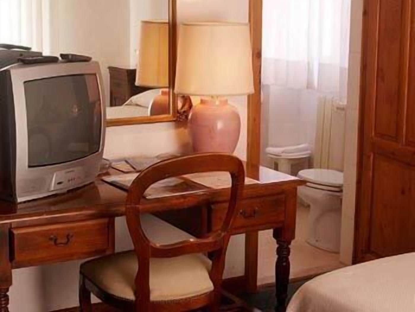 A hotel room with a wooden desk, a television, a lamp, and a bed.