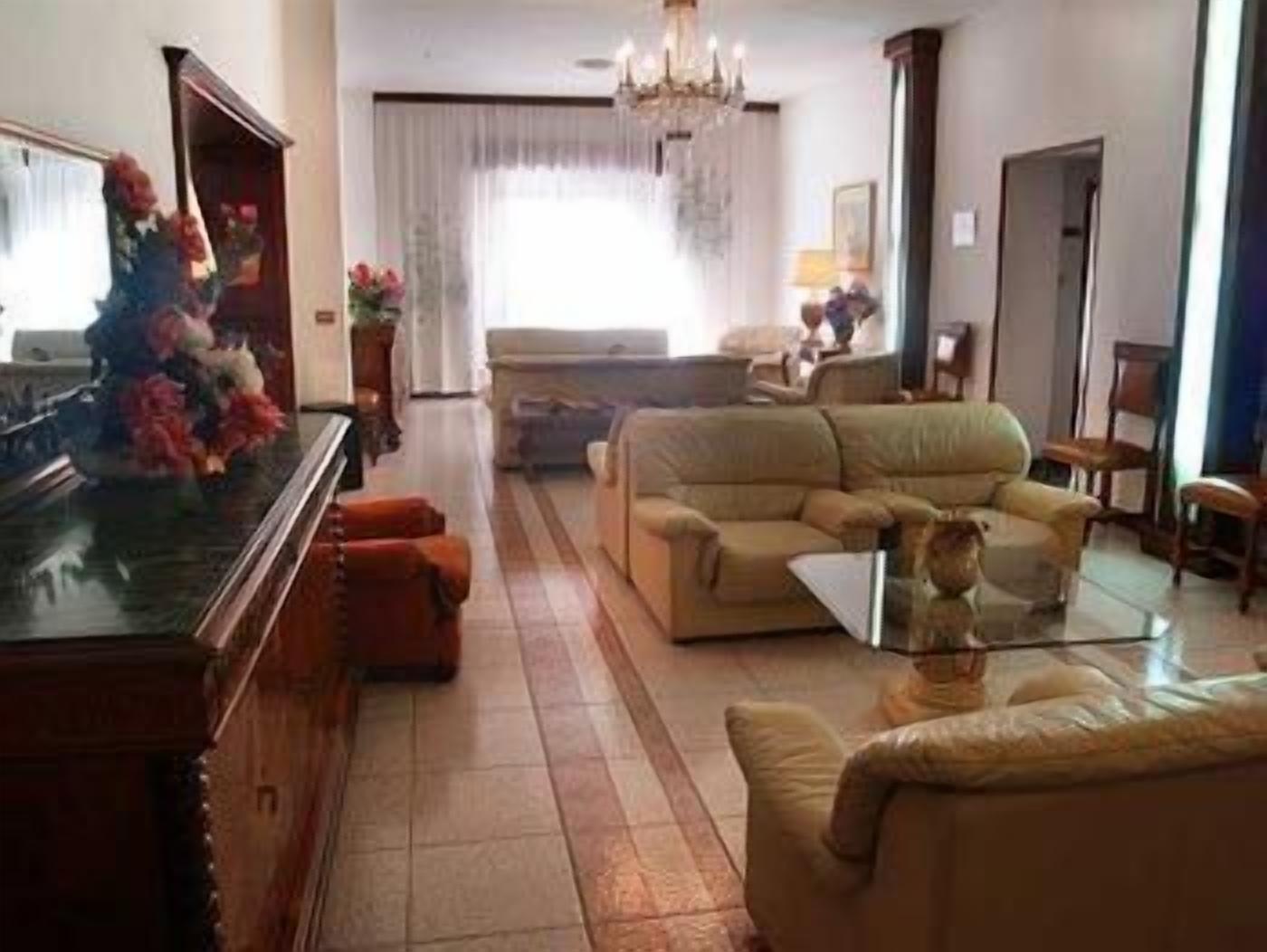 Ein Wohnzimmer mit einer Couch, einem Couchtisch und einem Fernseher. Eine Pendelleuchte und ein Fenster mit Vorhängen sind ebenfalls vorhanden.