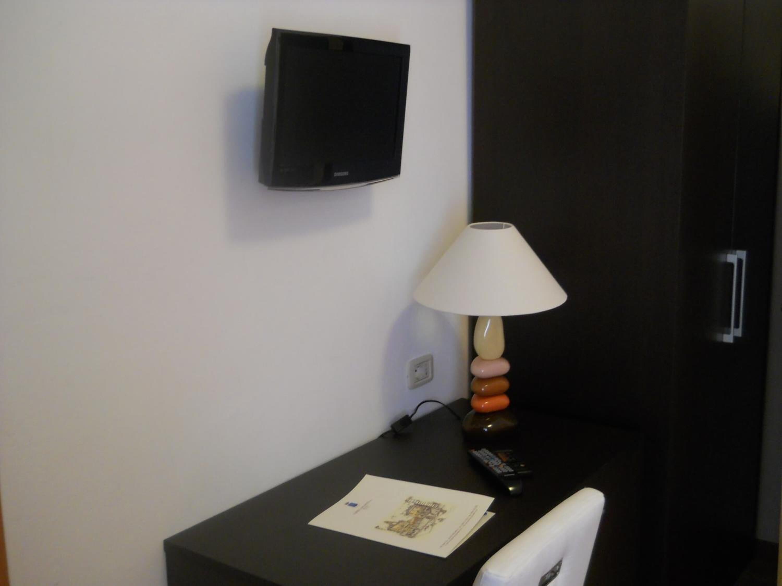 Un petit bureau avec une lampe, une télécommande et une feuille de papier.