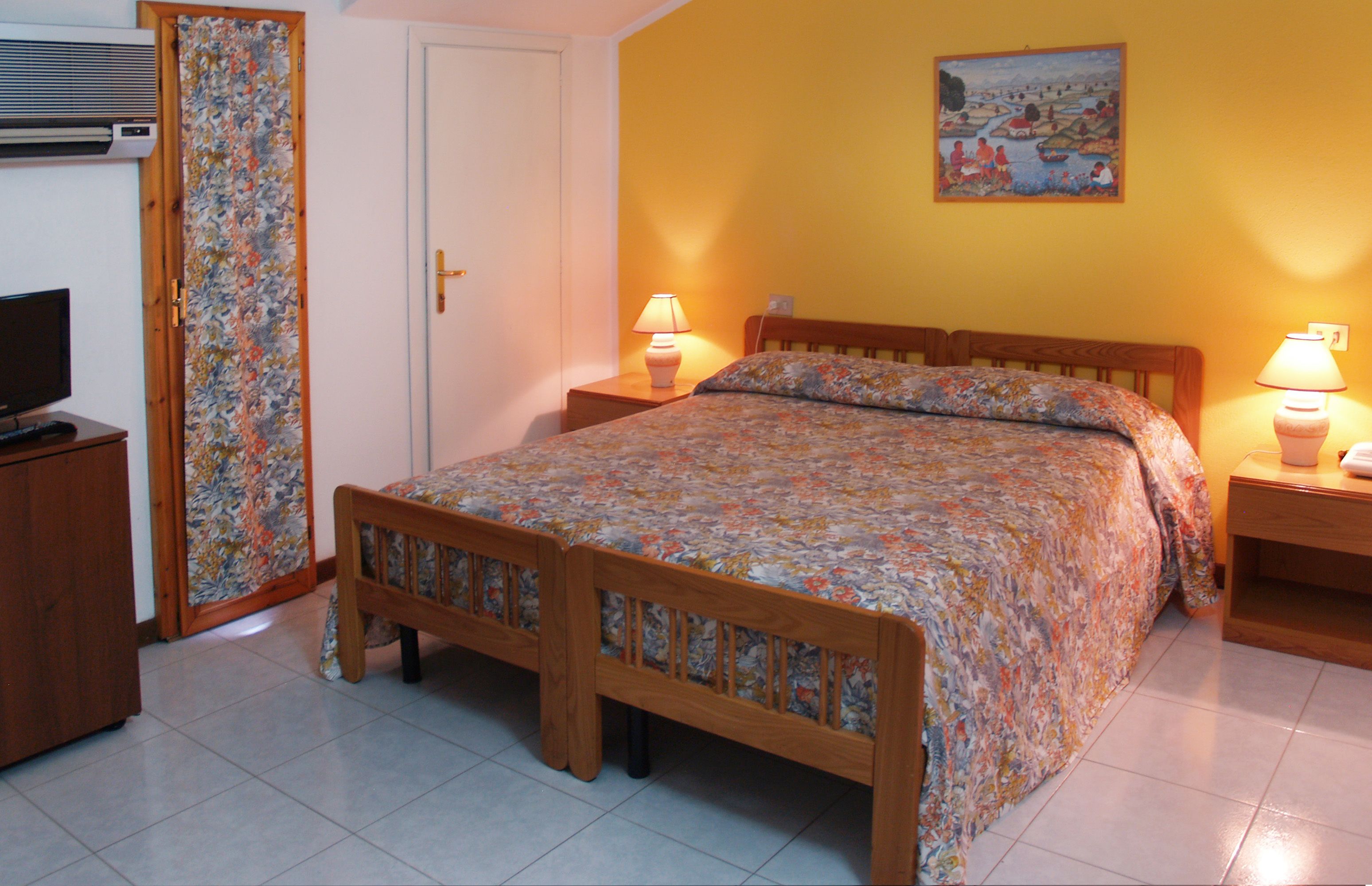 A bedroom with a wooden bed, two bedside lamps, a television, and a door with a floral curtain.