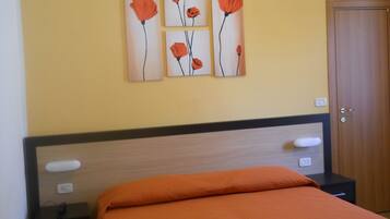 A bedroom with a bed, a nightstand, a wall-mounted artwork of red flowers, and a door.