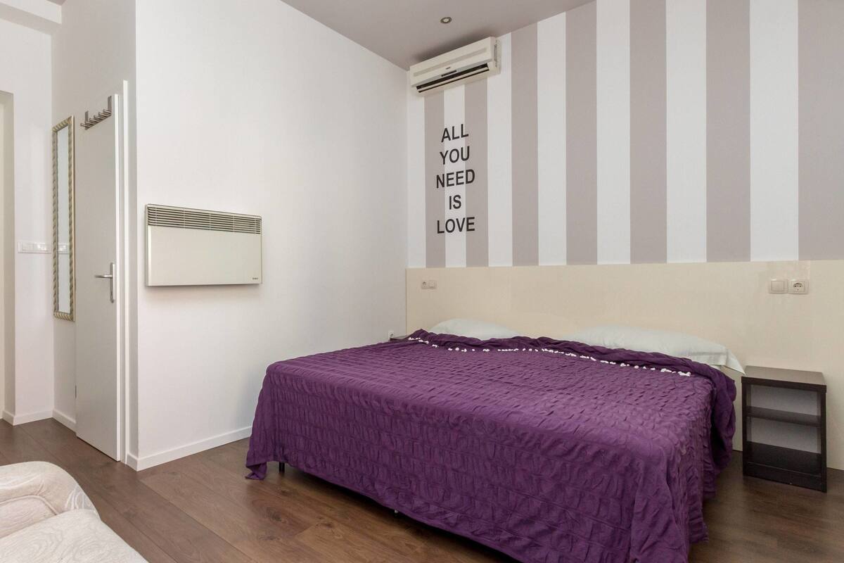 A bedroom with a bed, a mirror, a wall-mounted air conditioner, and a motivational quote on the wall.