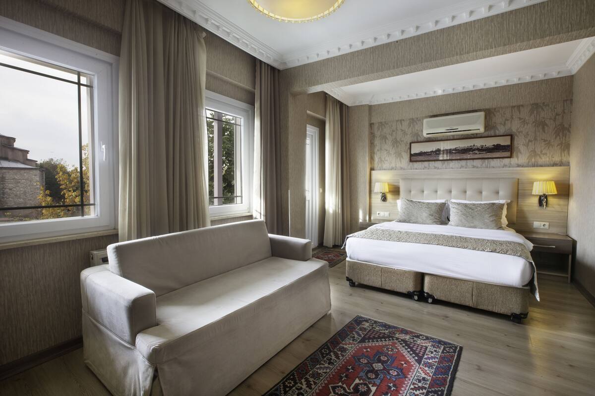 A hotel room with a bed, a sofa, a rug, and a window with curtains.
