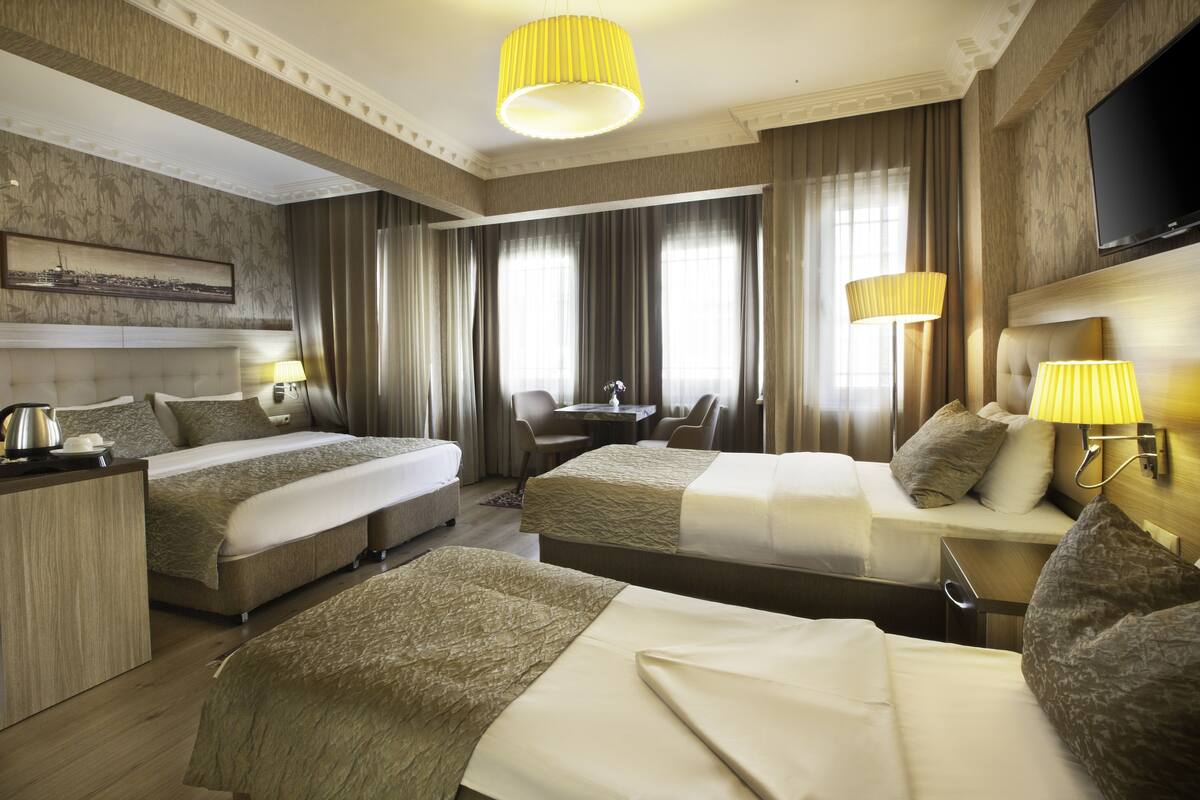 A hotel room with two beds, a desk, a chair, a television, and a window with curtains.