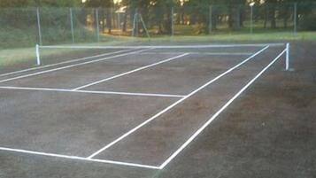 Una cancha de tenis al aire libre con líneas divisorias blancas y una valla.