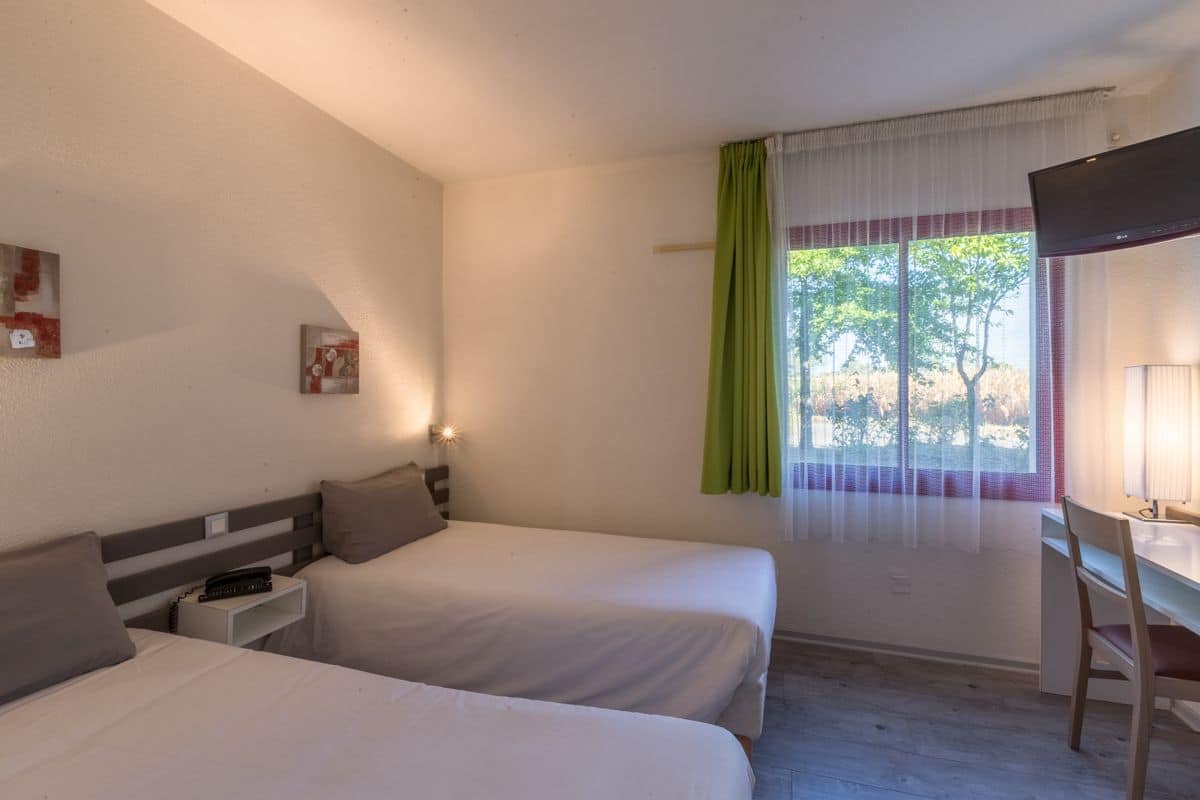 Une chambre avec deux lits, un bureau et une fenêtre avec des rideaux.