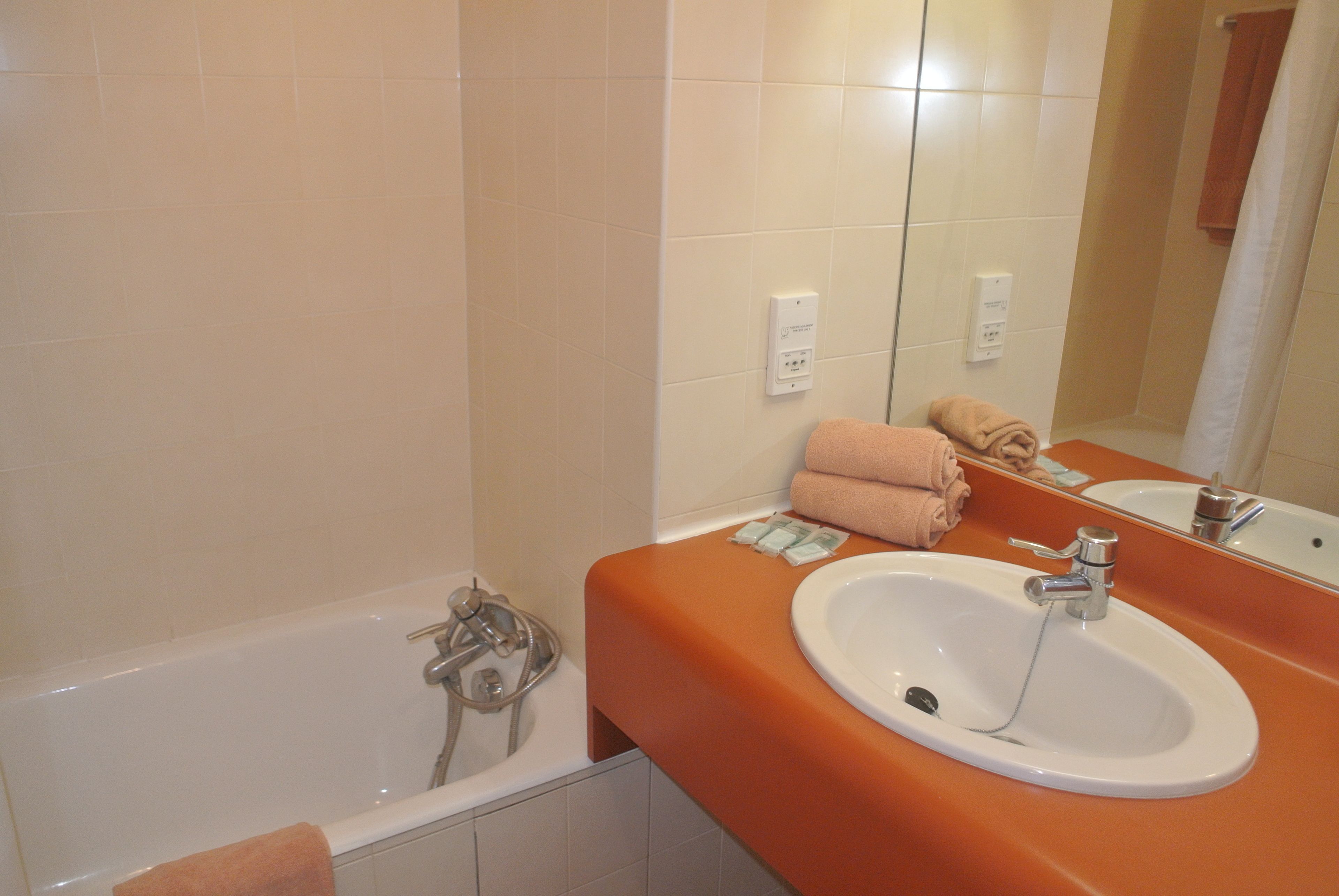 A bathroom with a bathtub, an orange sink, and a mirror.