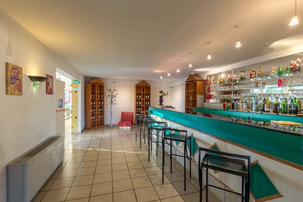 Una zona de bar con mostrador, taburetes y estantes llenos de botellas.