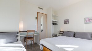 A hotel room with a bed, a desk with a chair, a wardrobe, and a mirror.