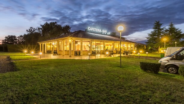 A well-lit outdoor cafe with a sign reading "CAFETERIA - BAR" and a self-service bar area.