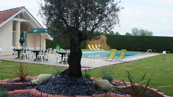 A backyard with a swimming pool, outdoor seating, and a large tree.