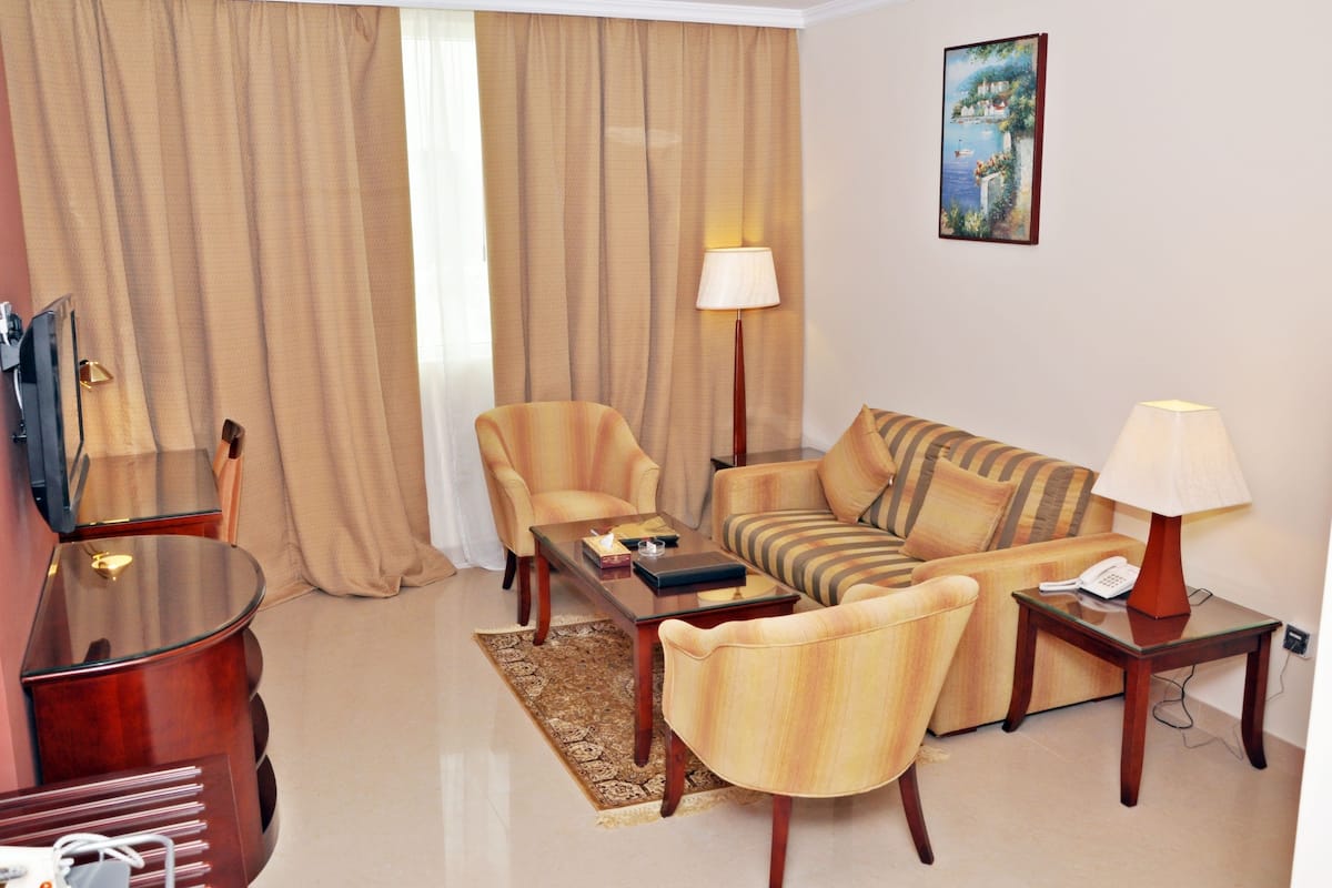 A hotel room with a sofa, armchairs, a coffee table, a TV, and a lamp.