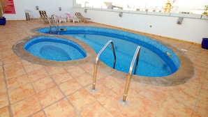 A swimming pool with two distinct sections, surrounded by lounge chairs and potted plants. - Ramee Royal Hotel Apartments (Abu Dhabi)