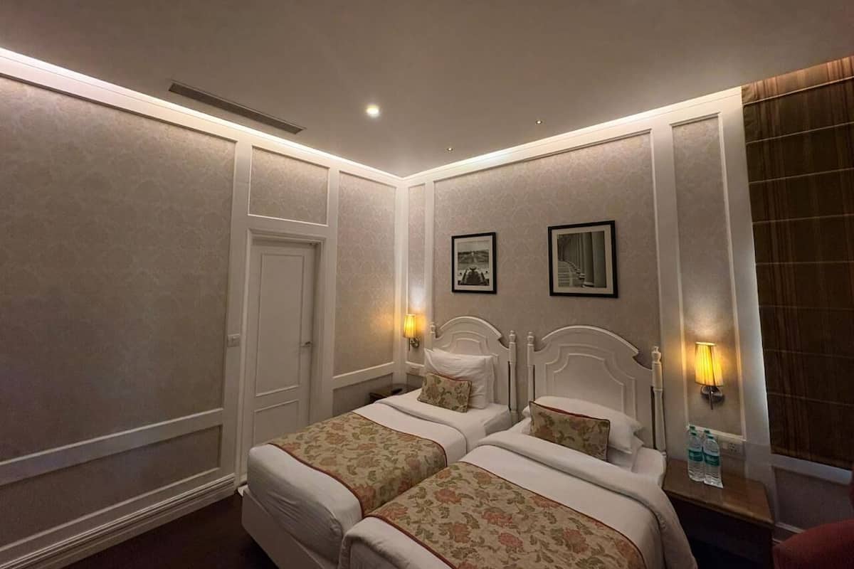 A hotel room with two beds, a wardrobe, a nightstand with a lamp, and a window with curtains.