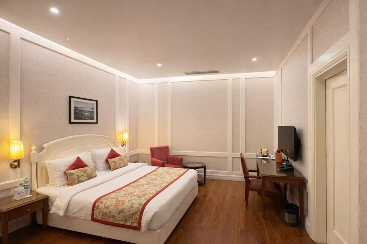 A hotel room with a bed, bedside table, lamp, chair, desk, TV, and a small table.