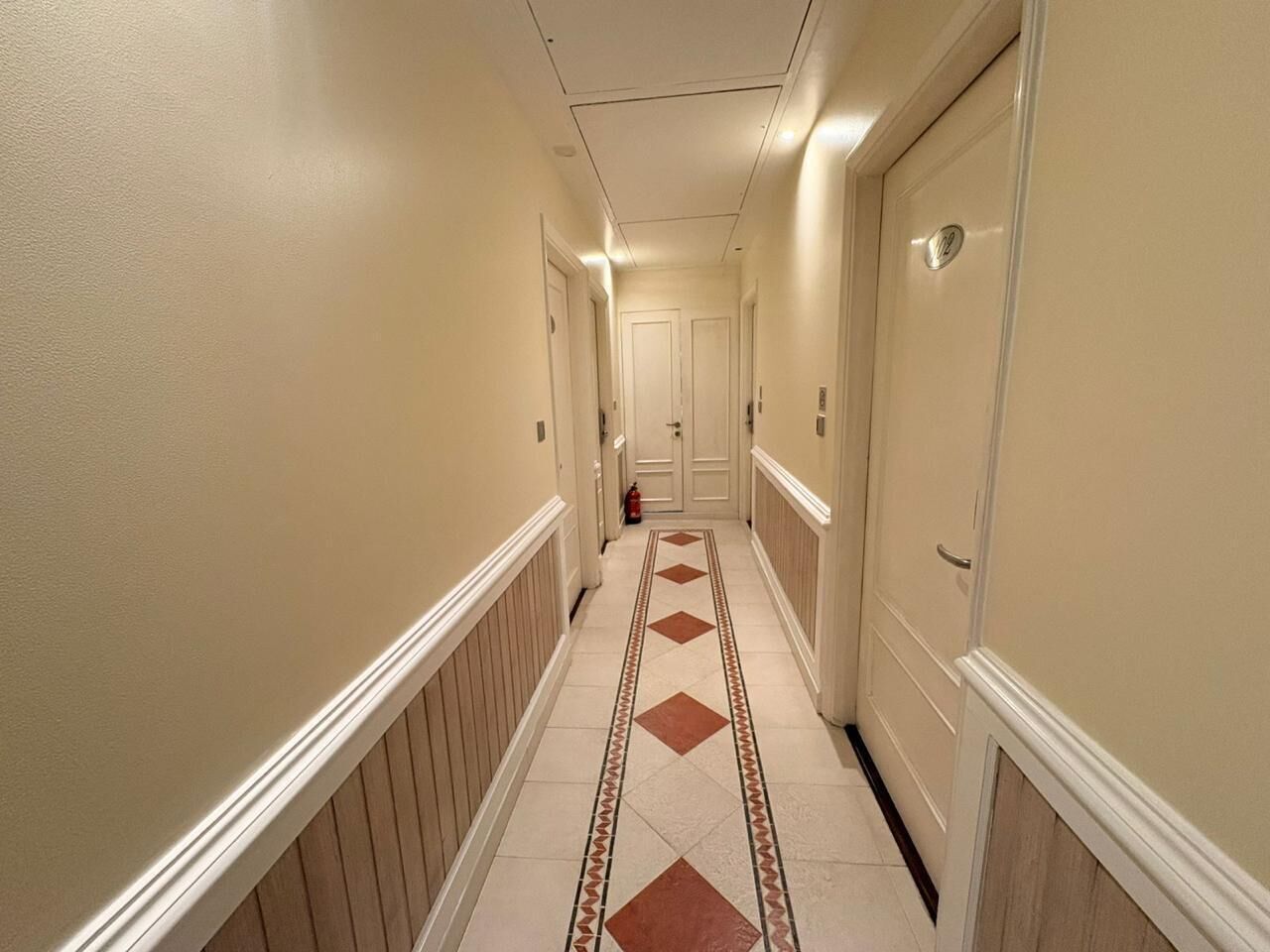 A hotel hallway with a tiled floor, white walls, and doors on both sides.