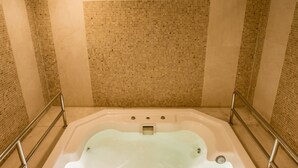 Ein großes, quadratisches Whirlpoolbecken mit Glasboden, umgeben von beige gefliesten Wänden und einer Metallumrandung.