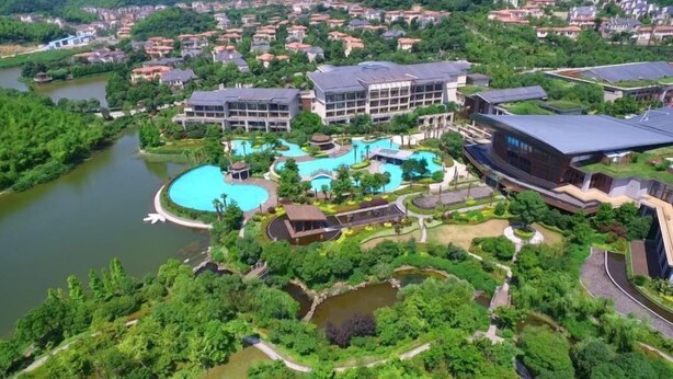 Un resort con varias piscinas, un edificio grande de diseño moderno y abundante vegetación alrededor.