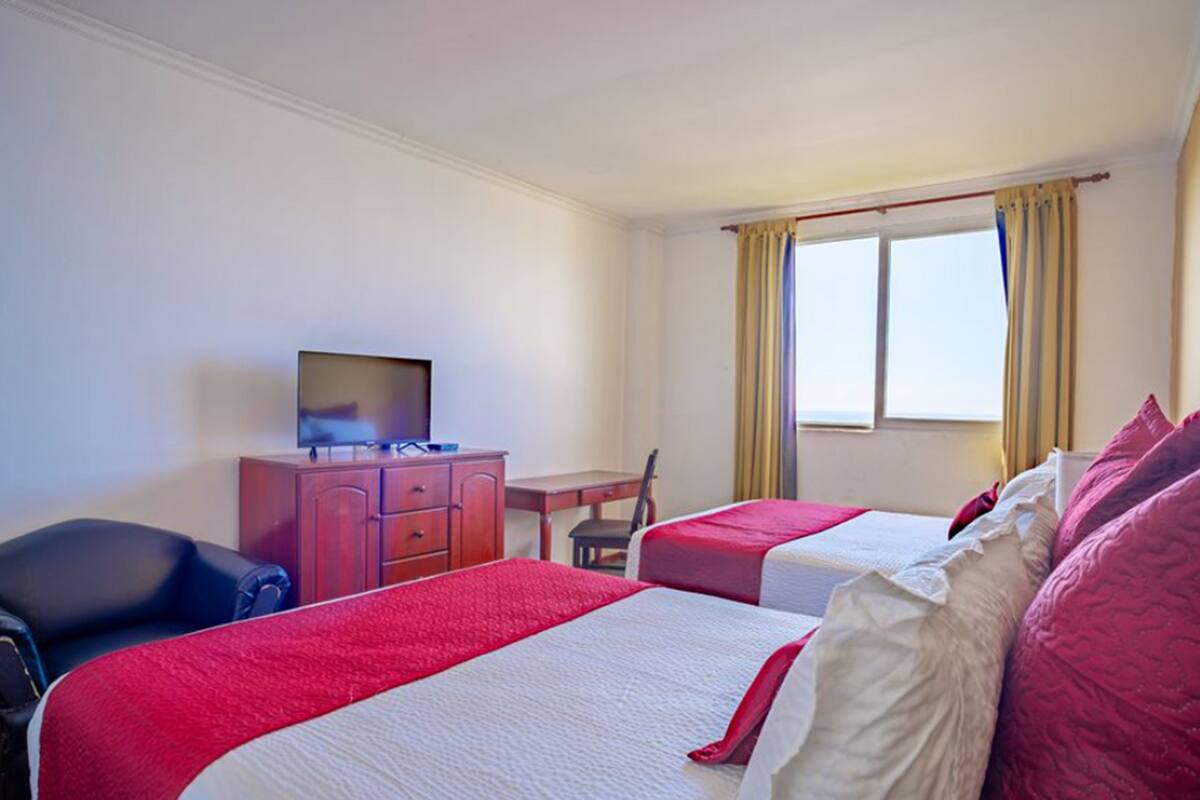 A hotel room with two beds, a desk, a television, and a chair.
