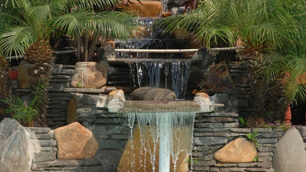 Una piscina amb cascada, envoltada de plantes tropicals i roques.