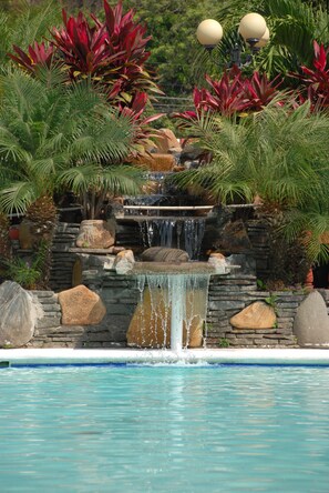 Una piscina con una cascada rodeada de plantas tropicales y rocas.