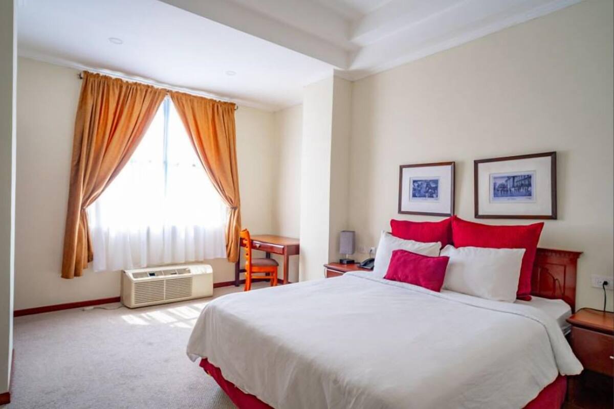 A hotel room with a large bed, a desk, and two framed pictures on the wall.