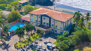 Vista aèria d'un hotel a la costa amb piscina, diversos edificis i una platja.