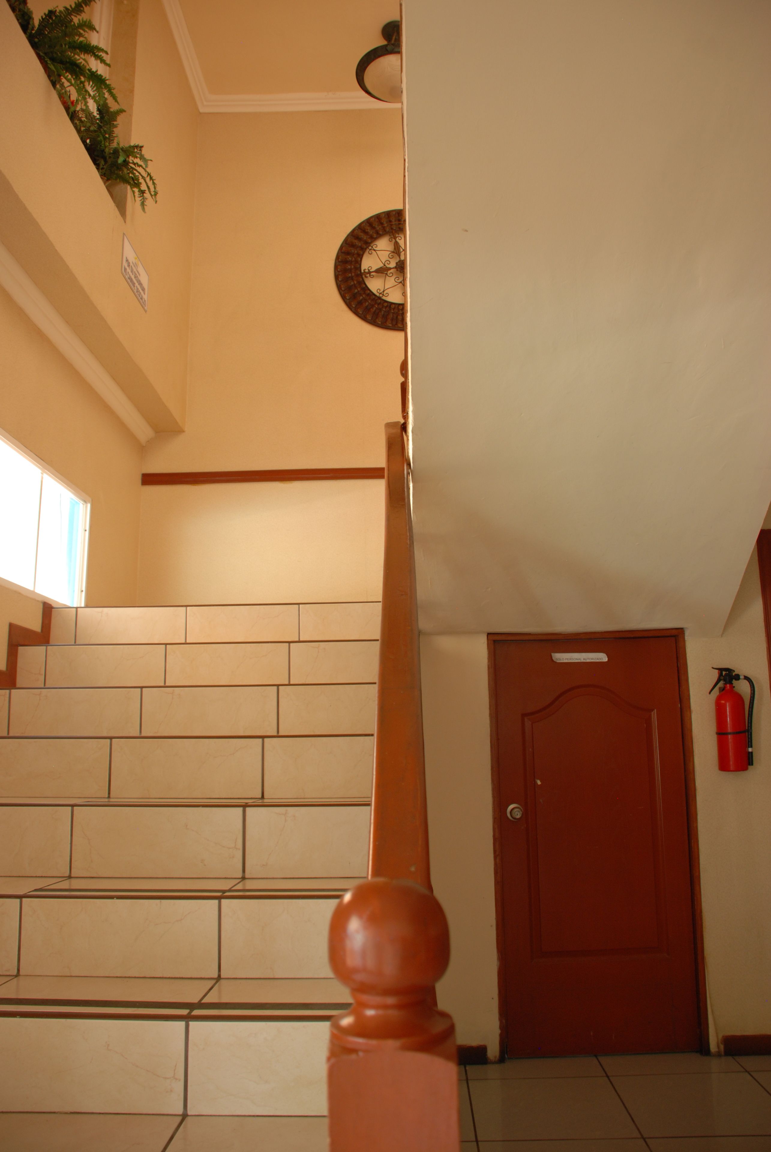 Una escalera con barandilla de madera, un extintor en la pared y una puerta cerrada.