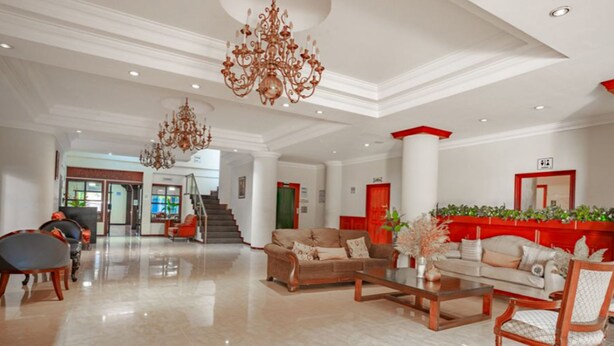 A spacious lobby with a grand chandelier, a staircase, and a reception area with red accents.