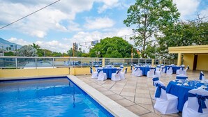 A poolside area with tables set for an event, a clear sky, and a view of a mountain in the background.