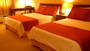 A hotel room with two beds, each with a red-striped bedspread, a desk with a chair, and a bedside table with a lamp and phone.