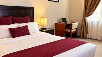Una habitación de hotel con una cama grande, un escritorio con una computadora portátil y dos cuadros en la pared.