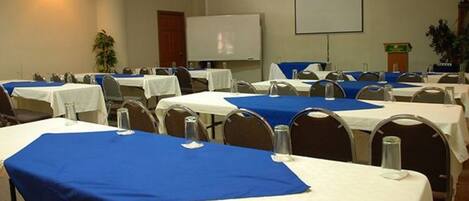 A conference room with tables set for meetings, a projector screen, and a whiteboard.